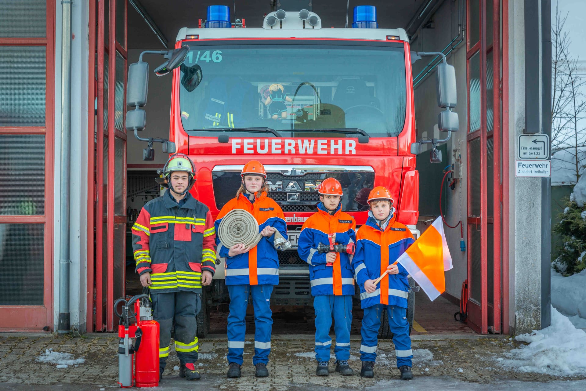 Vier Mitglieder der Jugendfeuerwehr in Einsatzkleidung vor dem HLF 1/46